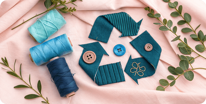 Eco-friendly sewing materials including teal and blue threads, fabric swatches, and buttons arranged with green plant elements